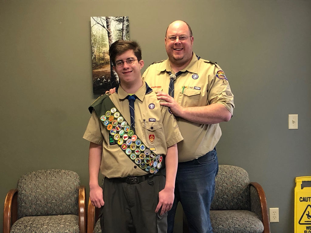 Image of Student Bryce Bernard with his father, wearing a brown boy scout shirt and a sash with badges.