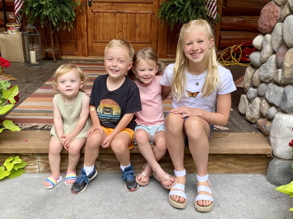 four young children sitting on front steps of a house