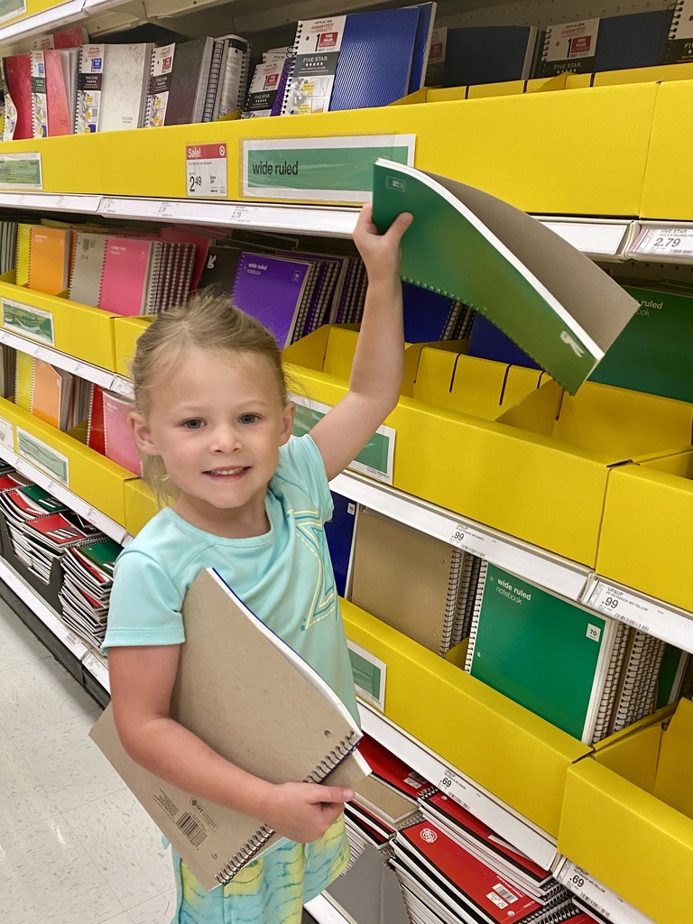 A young girls holding up a notebook in a store aisle of school supplies
