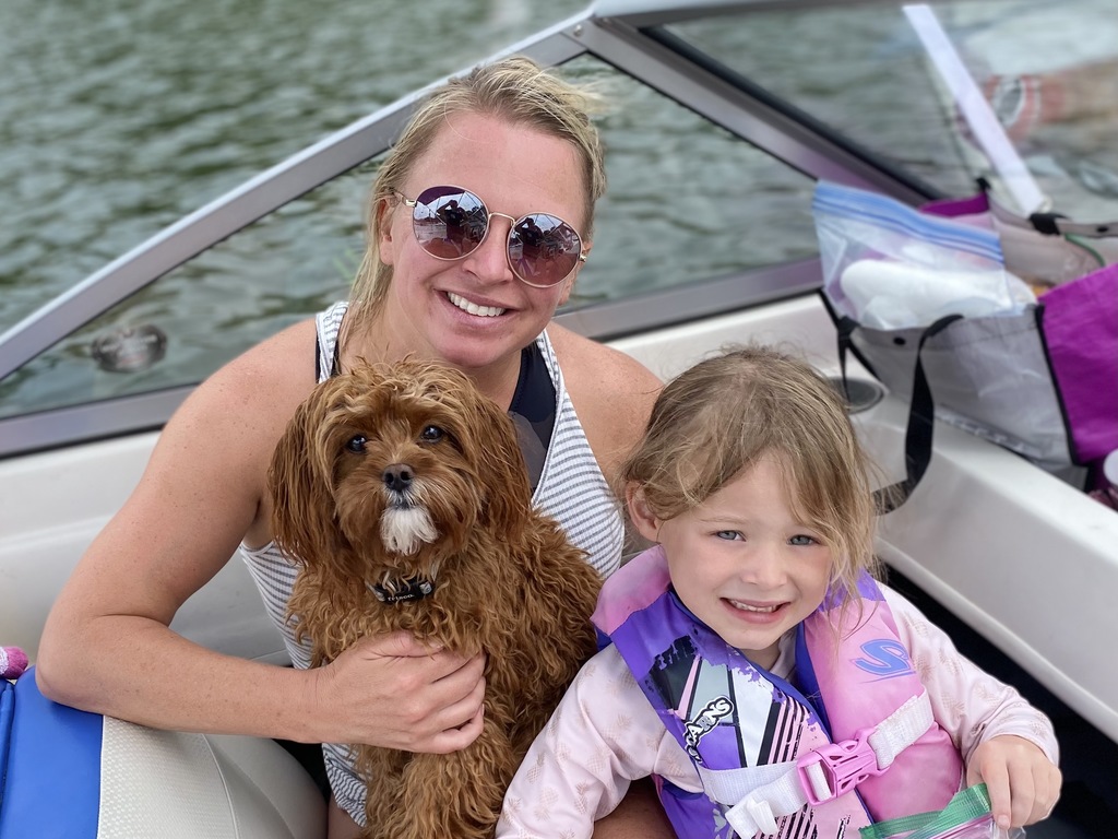 A woman holding a dog and young girl on lap on a boat in a lake