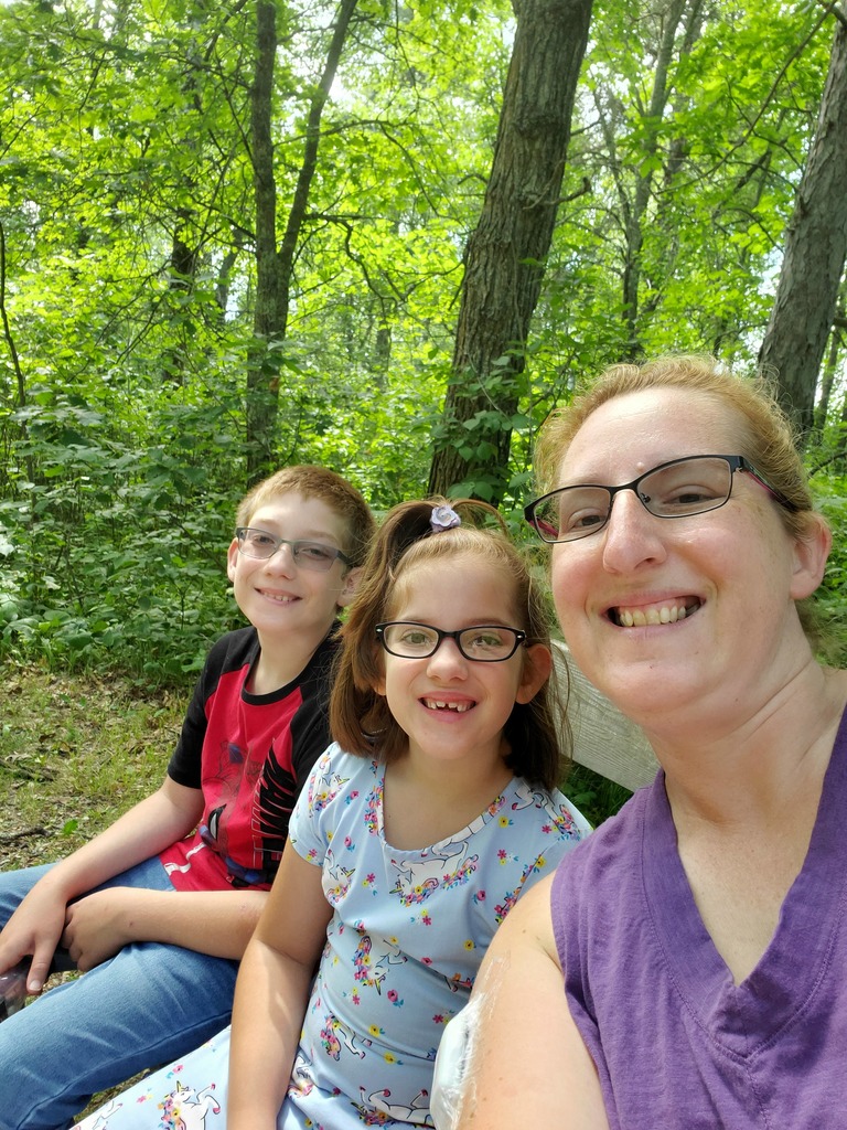 Woman and two children selfie in front of wooded area