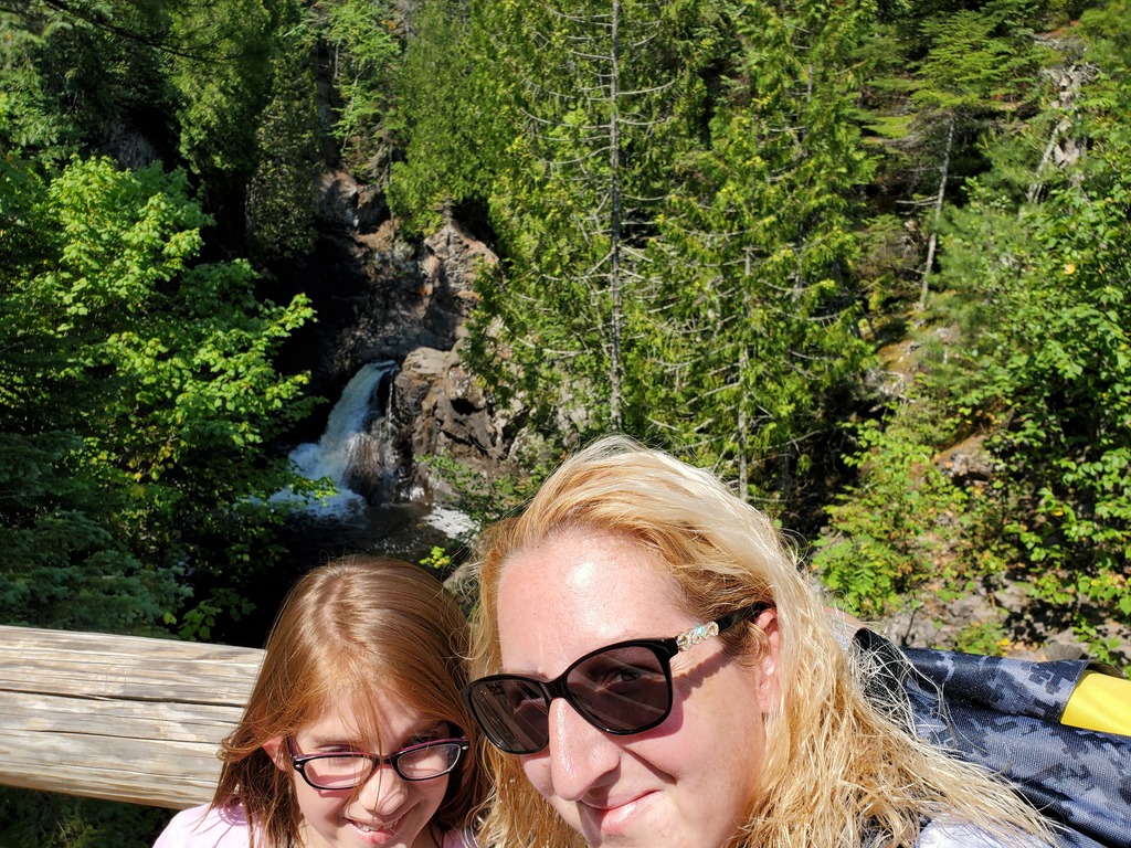 Woman and young girl in front of a small waterfall and forested area