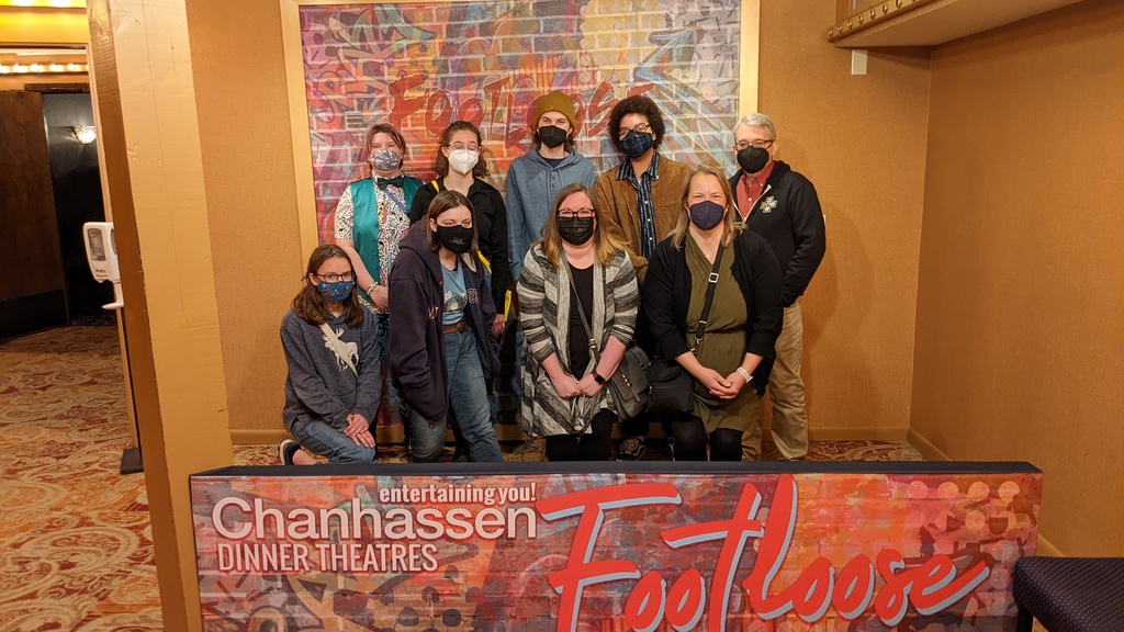 9 individuals posting in front of a colorful wall behind a banner than reads: "entertaining you Chanhassen Dinner Theatres Footloose"