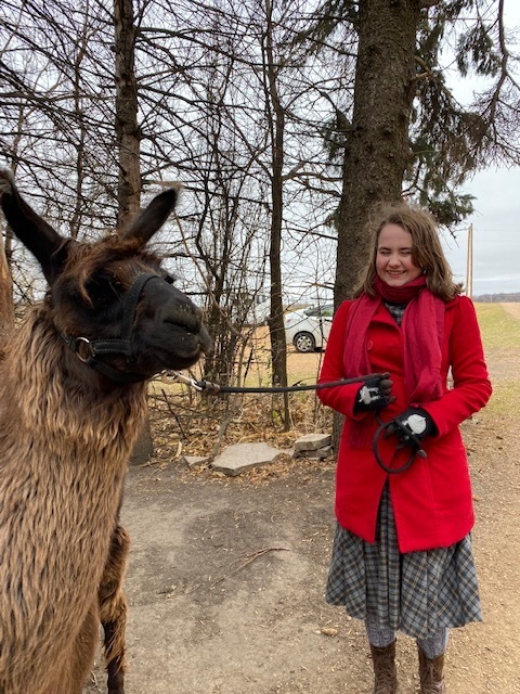 Image of a student in a red coat holding the reigns of a llama. 