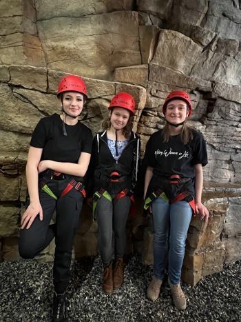 Image of students in red helmets and climbing gear in front of a climbing course