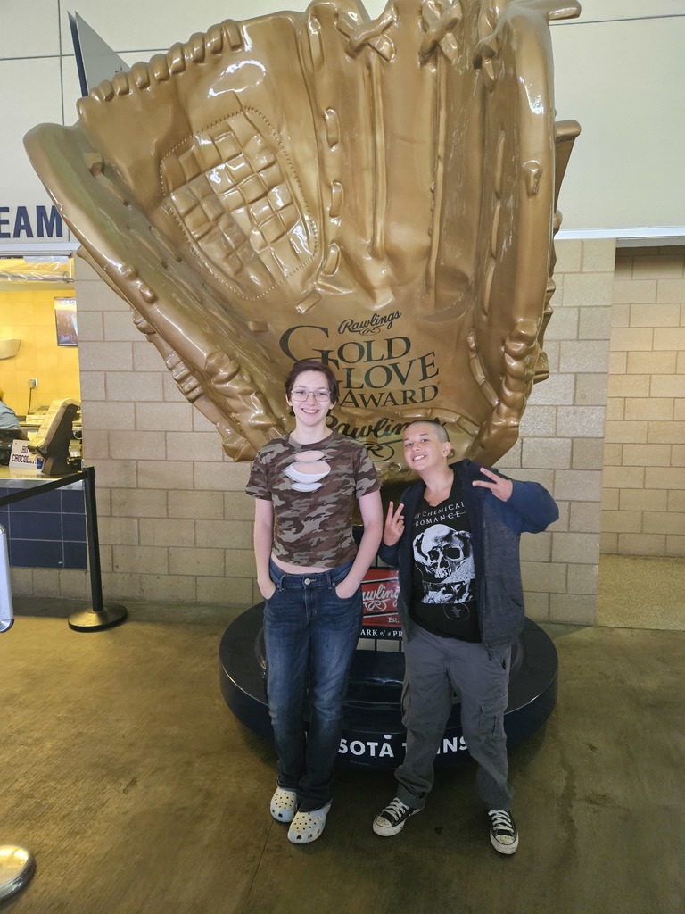 two students in front of a large baseball glove statue